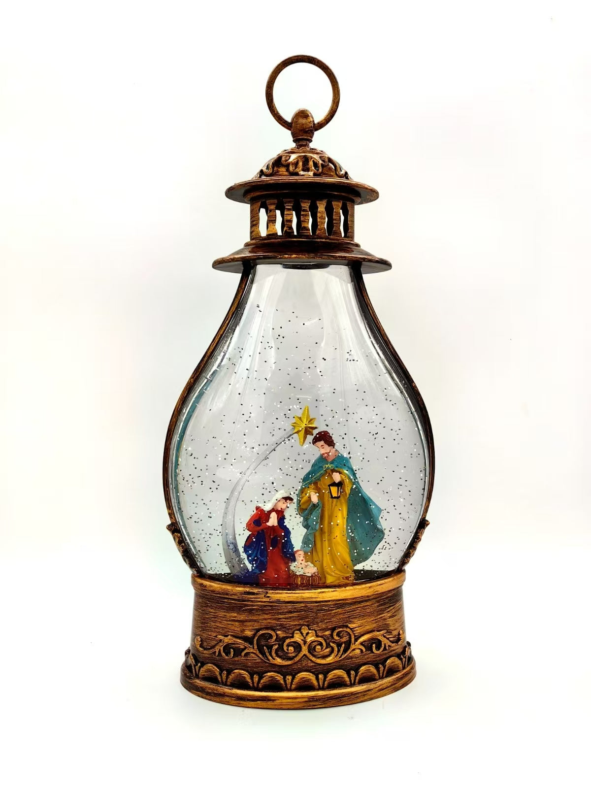 A decorative lantern-shaped snow globe with an ornate bronze-toned metal frame, clear glass body, and miniature nativity scene inside featuring a yellow star and figures in colorful robes.