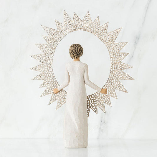 A decorative figurine of a woman seen from behind, wearing a long white gown and holding a large sunburst frame made of openwork geometric segments. The background is a clean white marble surface and wall.