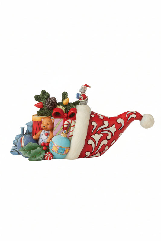 A Christmas-themed figurine shaped like a Santa hat filled with holiday gifts, a teddy bear, a blue ornament, pinecones, holly, and a small Santa figure, shown on a plain white background.