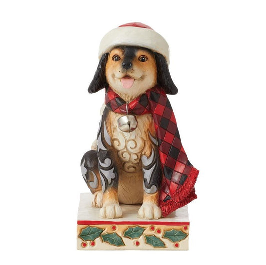 A decorative figurine of a dog wearing a Santa hat and a red plaid scarf, sitting on a holly-accented base against a plain white background.