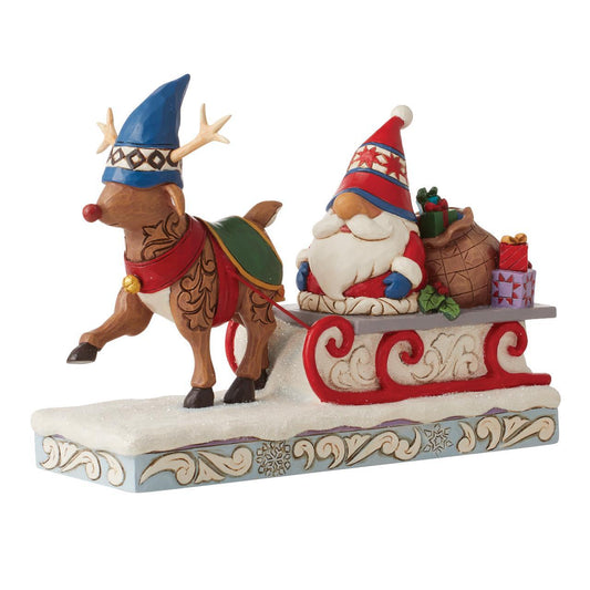 A decorative holiday figurine showing Santa Claus sitting in a red sleigh pulled by a brown reindeer wearing a blue hat, on a snowy base against a plain white background.