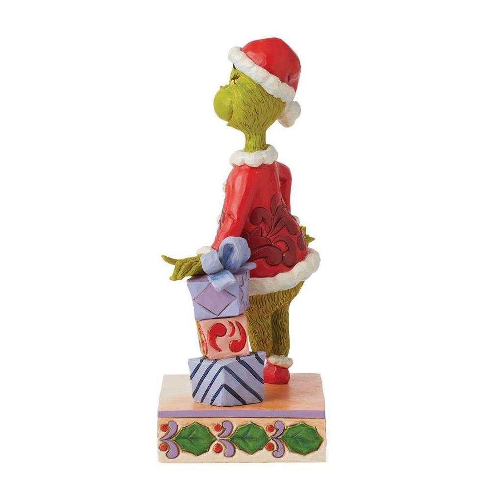 A Grinch figurine wearing a Santa hat and red sweater, standing on a decorated base with wrapped presents, photographed on a plain white background.