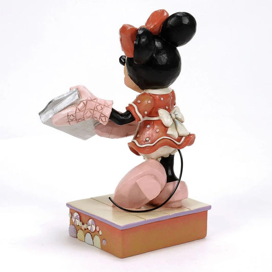 A decorative figurine of Minnie Mouse kneeling on a small tiled base and holding a silver gift box, shown against a plain white background.