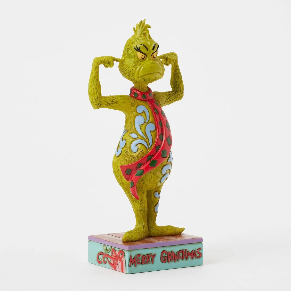 A Dr. Seuss Grinch figurine standing on a decorative base that reads 'Merry Christmas,' photographed against a clean white background.