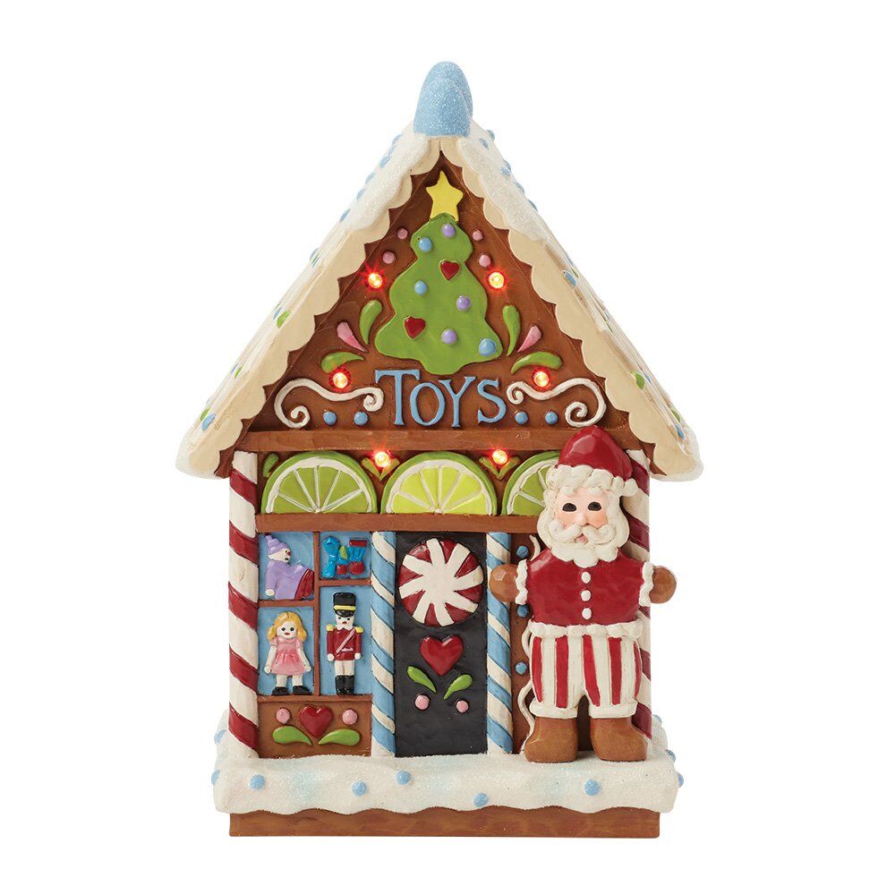 A gingerbread-style decorative house ornament labeled 'Toys' with a Santa Claus figure standing beside it, shown on a plain white background.