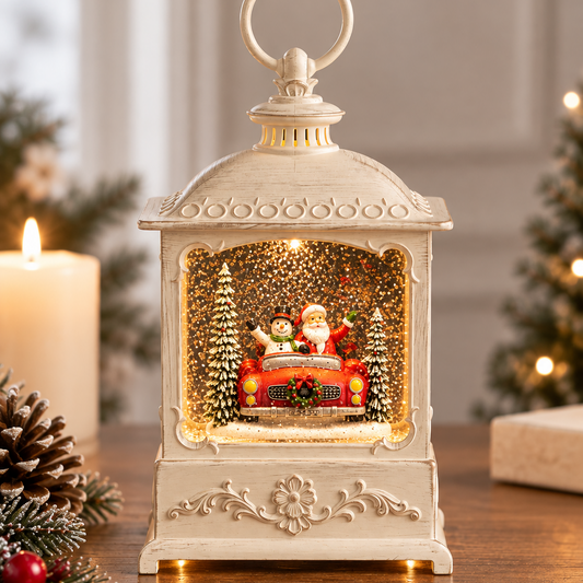 An ornate cream-colored lantern-shaped Christmas ornament sits on a wooden table, glowing with warm light from within. The lantern features a Santa Claus and snowman scene with gold glitter and miniature trees.