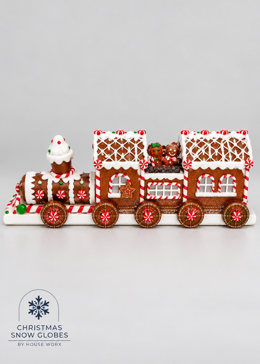 A gingerbread Christmas snow globe train decoration with white icing details, red and white candy cane accents, and small holiday figures, photographed on a light gray background. A logo at the bottom reads Christmas Snow Globes by House Work.