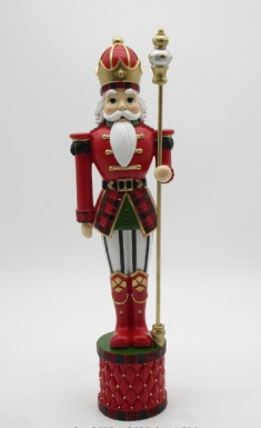 A traditional Christmas nutcracker figurine standing on a decorated base, wearing a red and black plaid uniform with gold trim, a white beard, and holding a gold staff.