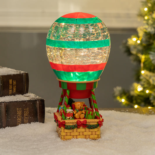 Decorative hot air balloon christmas snow globe with lights on a snowy surface, Christmas tree in the background
