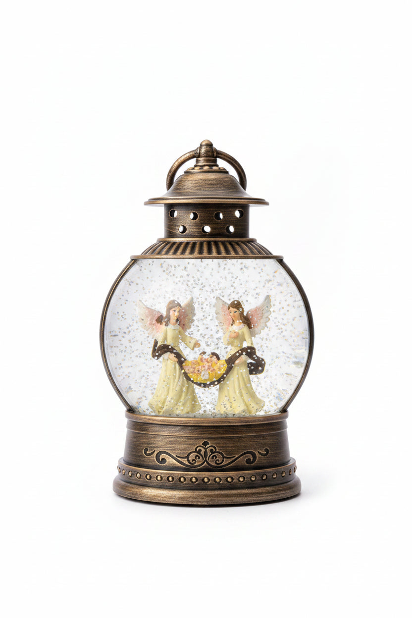 An antique-style snow globe lantern with a bronze-colored metal base and top, featuring two angel figures inside a clear glass sphere filled with glittery white snow, set on a dark granite countertop.