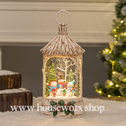 Decorative lantern with snowman scene in front of a Christmas tree, featuring Houseworx brand. Straw hut christmas snow globe