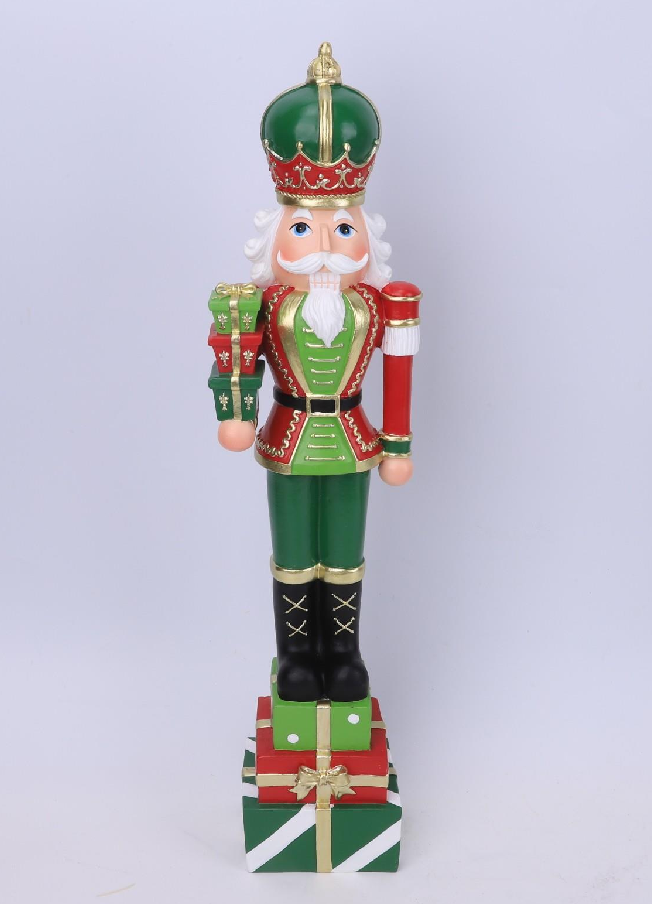 A festive Christmas nutcracker figurine standing on a box of wrapped gifts. The nutcracker is dressed in a green and red uniform with gold trim, a green and red crown, a white beard, and holds a red and gold staff.