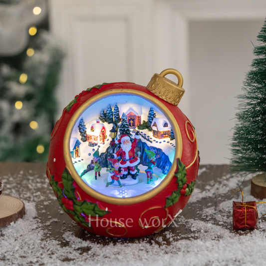 Decorative Christmas ornament with a lit scene of Santa Claus, surrounded by trees and houses, on a snowy surface.