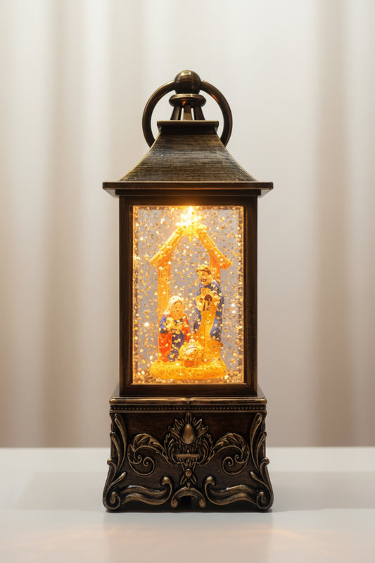 A decorative lantern-style night light with an ornate dark metal frame, glowing warm light, and a nativity scene inside, isolated on a white background.
