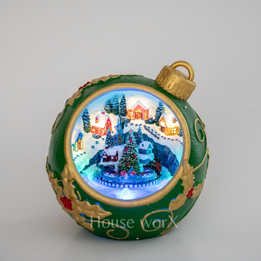 Decorative Christmas ornament with a miniature village scene inside, featuring green and gold colors.