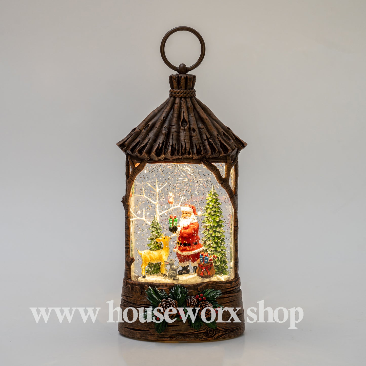 Decorative lantern with Santa Claus and Christmas trees inside, on a light gray background. Straw hut christmas snow globe