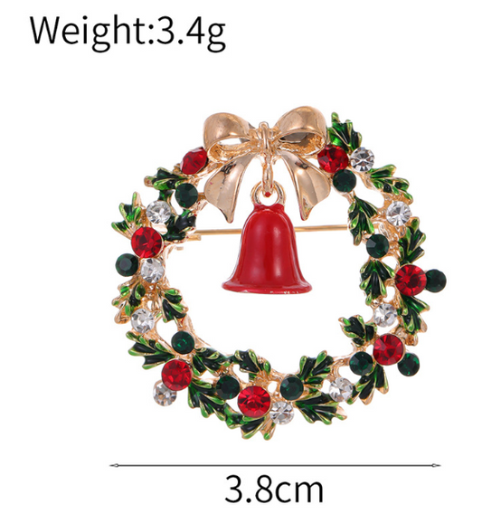A round Christmas-themed brooch with a red bell, green leaves, and red berries, with a gold-tone bow and bell ornament.