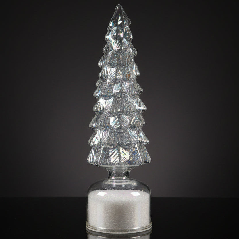 A small iridescent glass Christmas tree with a tiered design and a clear round base, standing on a kitchen countertop with a white sheet of paper behind it.