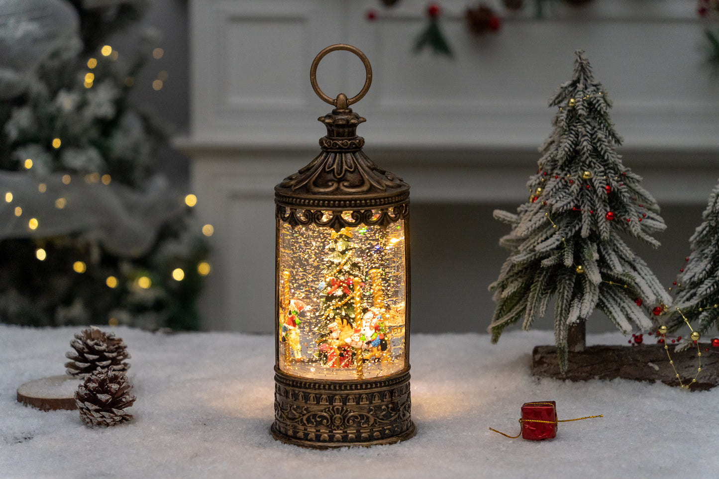 Decorative lantern with a small Christmas scene inside, surrounded by festive decorations on a snowy surface.