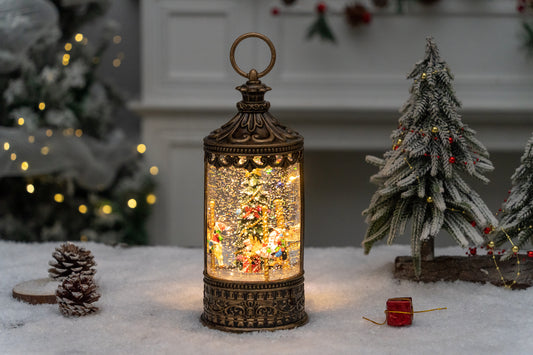 Decorative lantern with a small Christmas scene inside, surrounded by festive decorations on a snowy surface.