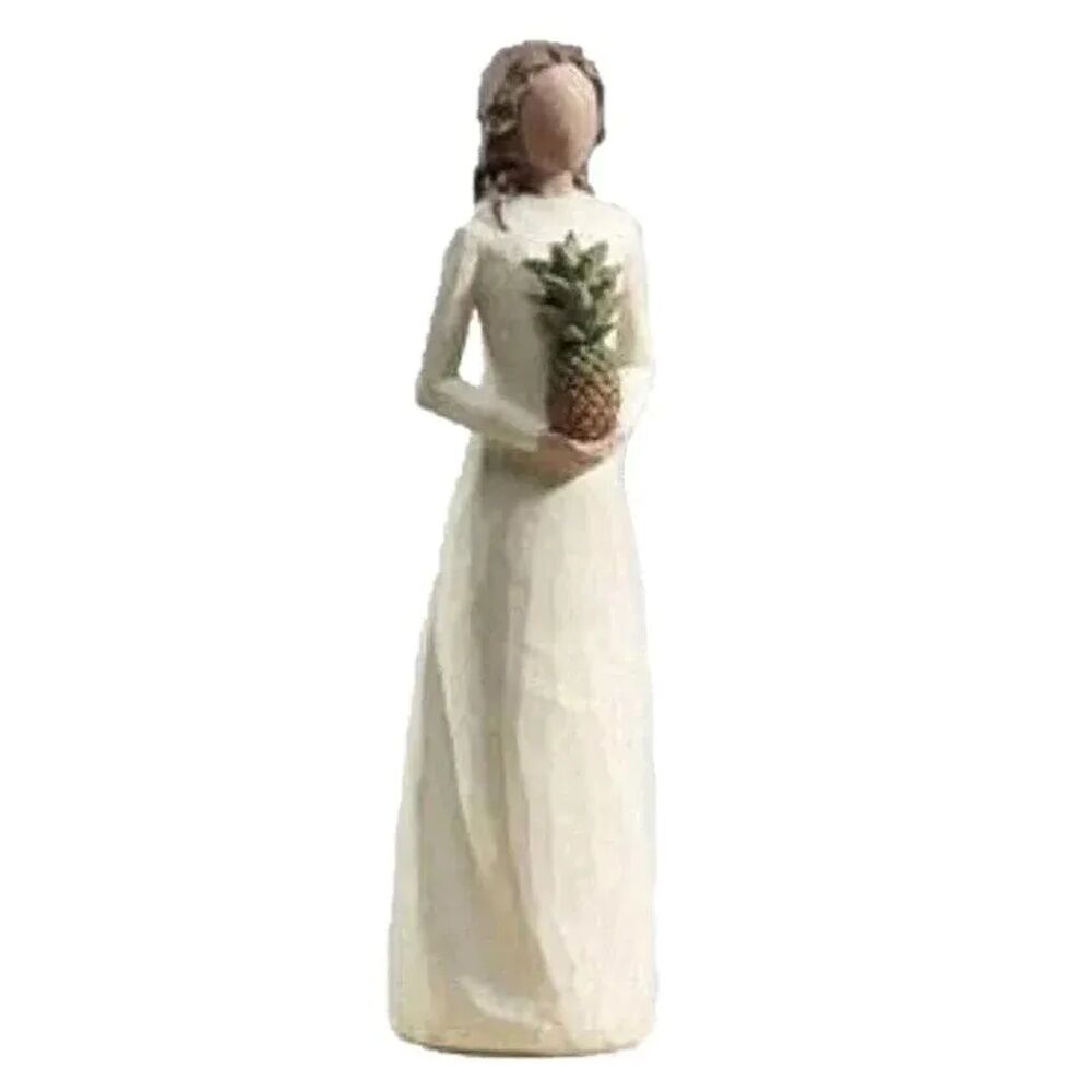 A Willow Tree figurine of a woman in a long cream dress holding a small pineapple, isolated on a white background.