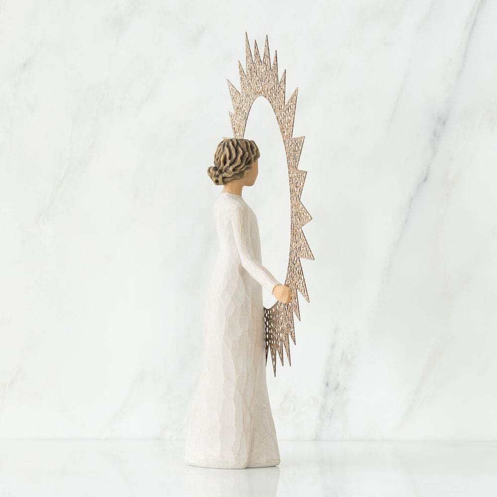 A Willow Tree figurine of an angel with a long white gown and patterned hair, holding a large gold sunburst mirror, set against a white marble background.