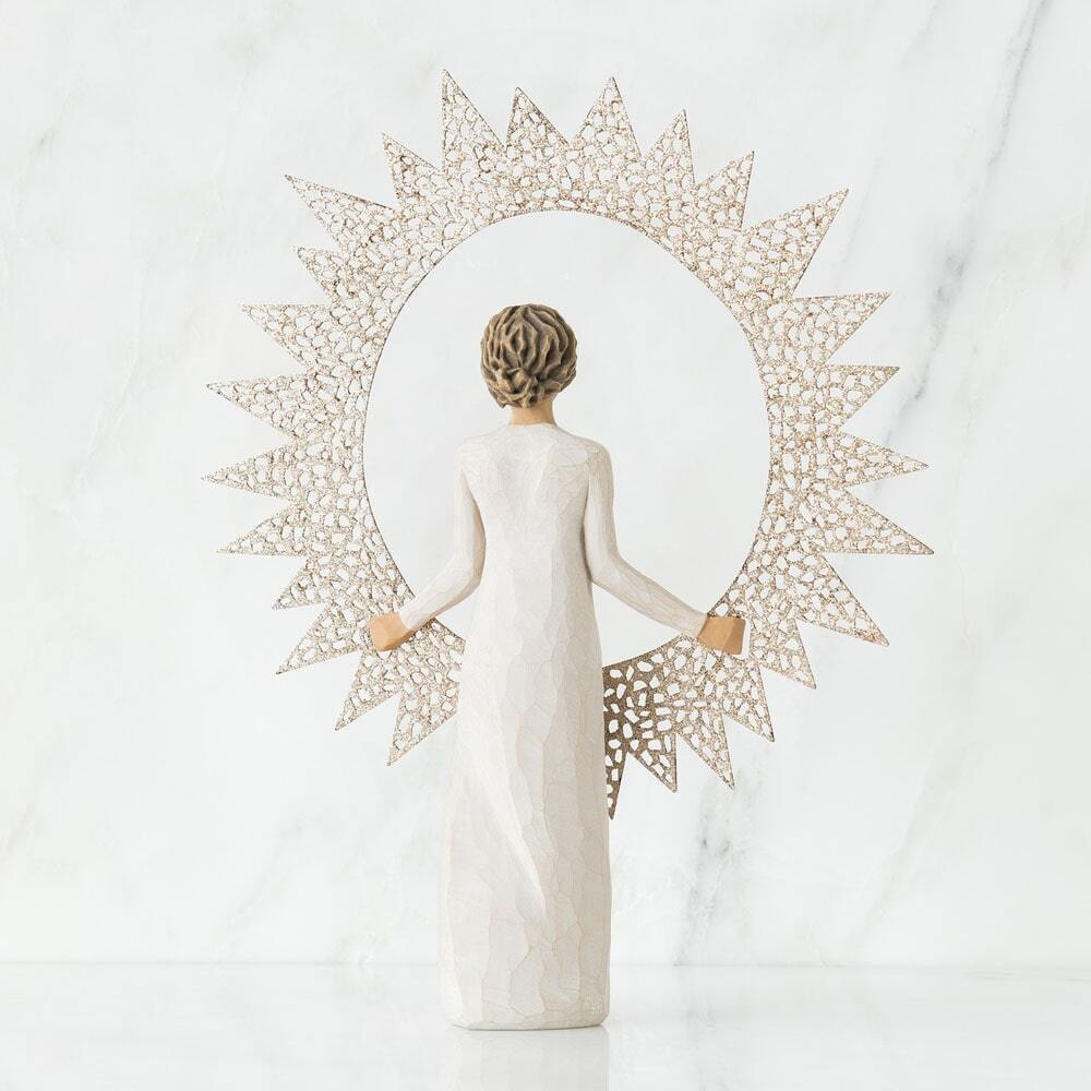 A decorative figurine of a woman seen from behind, wearing a long white gown and holding a large sunburst frame made of openwork geometric segments. The background is a clean white marble surface and wall.