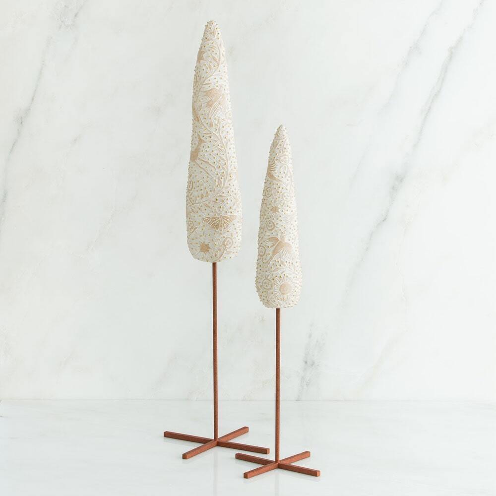 Two decorative tree-like sculptures with textured cream and gold patterned tops on slender brown metal stands, set against a white marble background.