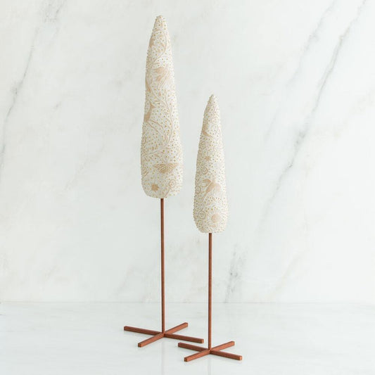 Two decorative tree-like sculptures with textured cream and gold patterned tops on slender brown metal stands, set against a white marble background.