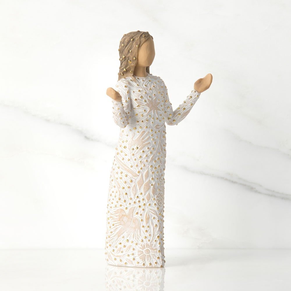 Statue of a woman in a long, white, lace dress with gold accents on a white background