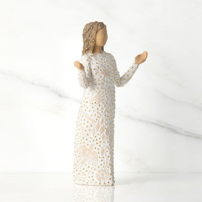 Statue of a woman in a long, white, lace dress with gold accents on a white background