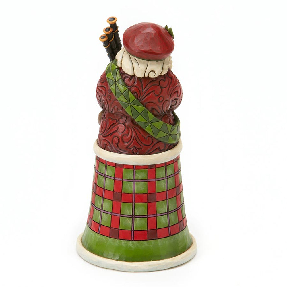 A decorative ceramic figurine of a Scottish bagpiper seated inside a bell-shaped body decorated with a red and green tartan pattern, on a plain white background.