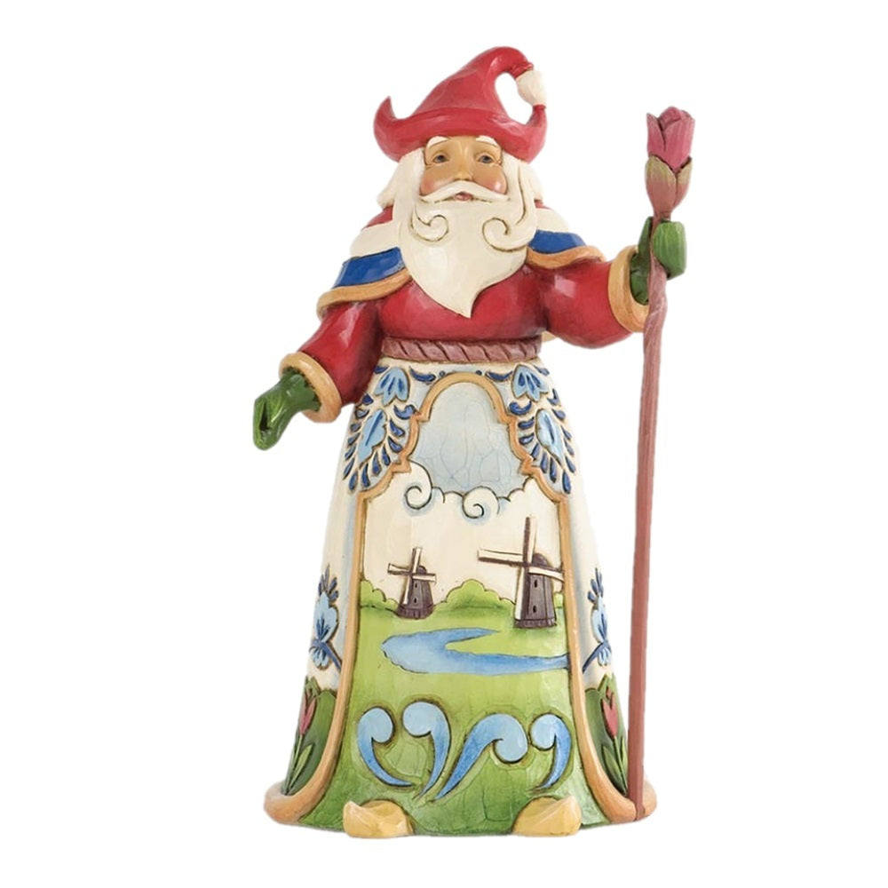 A traditional Dutch garden gnome figurine with a red hat and robe, white beard, and a painted landscape panel on the front, holding a pink flower bud on a staff, isolated on a white background.