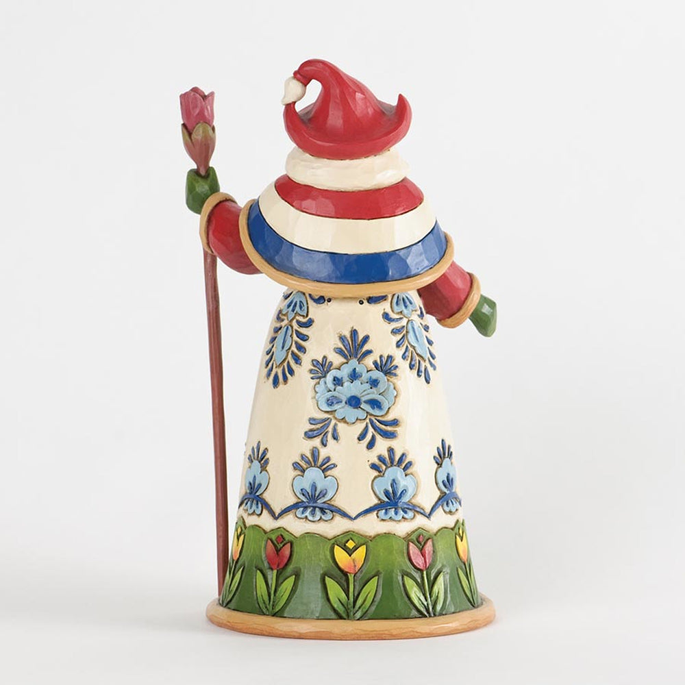 A hand-painted ceramic gnome figurine wearing a red, white, and blue striped hat and coat with blue floral patterns on a cream dress, holding a red rose on a staff.