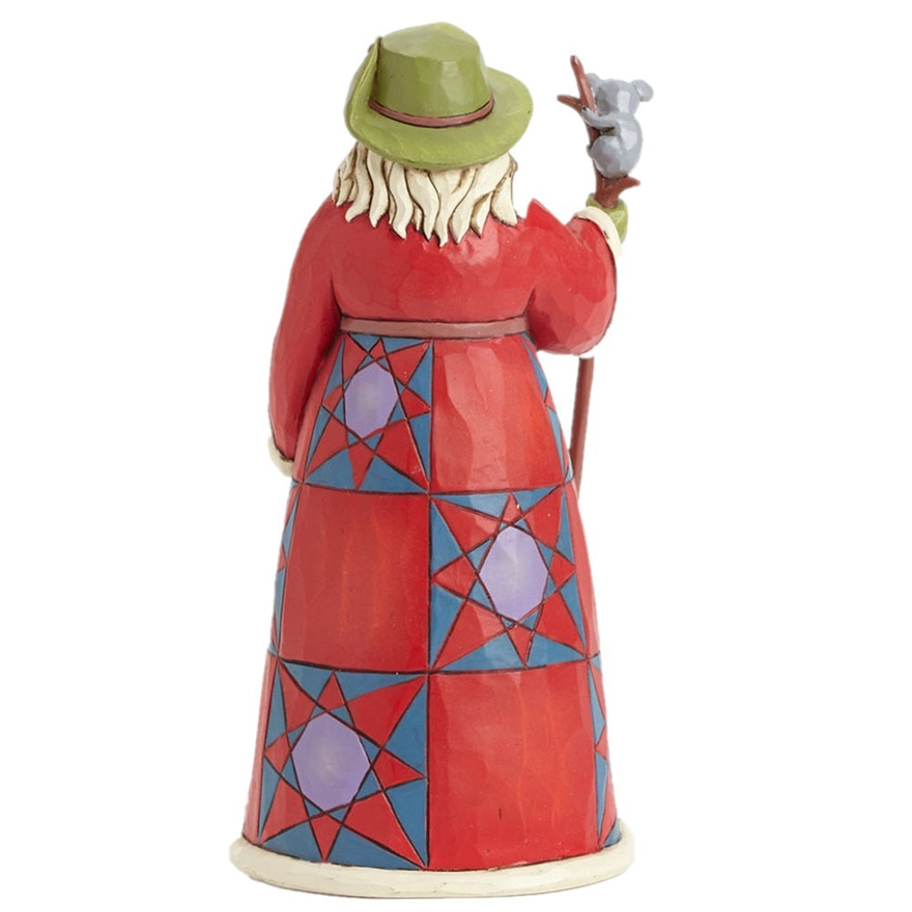 A hand-painted figurine of a Santa Claus-like figure seen from the back, wearing a red robe with blue and purple geometric star patterns, a green hat, and holding a staff with a small gray animal.