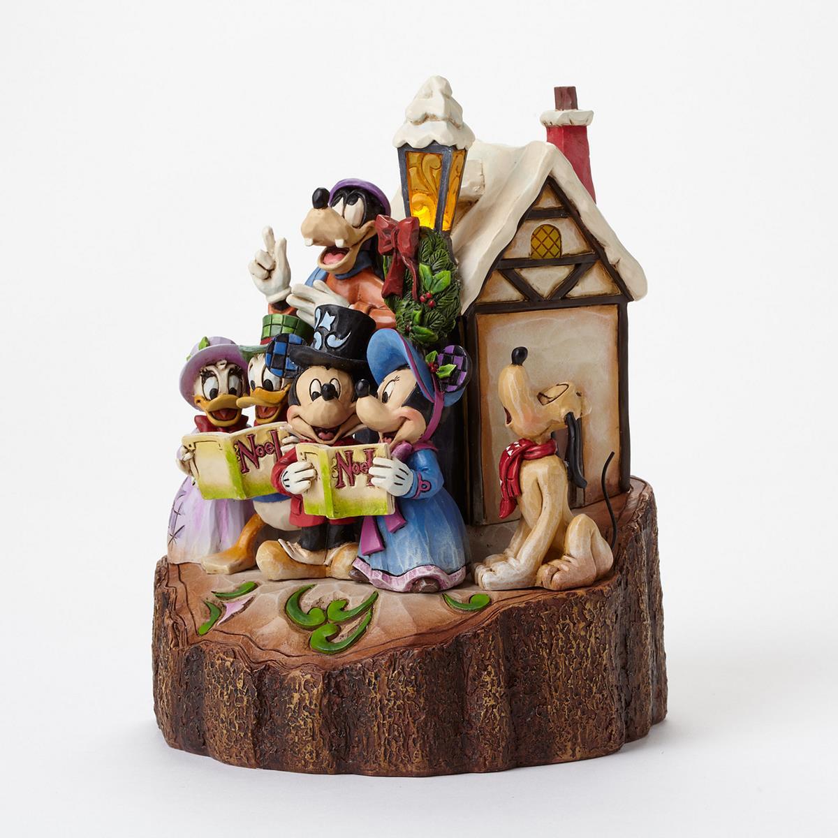 A Disney holiday figurine set featuring Mickey, Minnie, Goofy, Pluto, and Daisy in a snowy cottage scene on a log base, photographed against a clean white background.