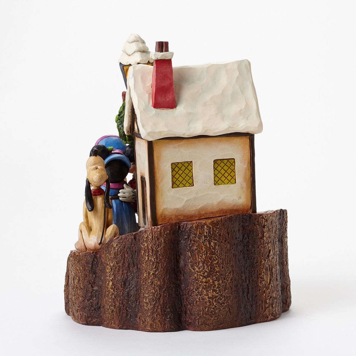 A decorative figurine of a small house on a tree stump base, with cartoon characters and a dog standing beside it, photographed against a plain white background.