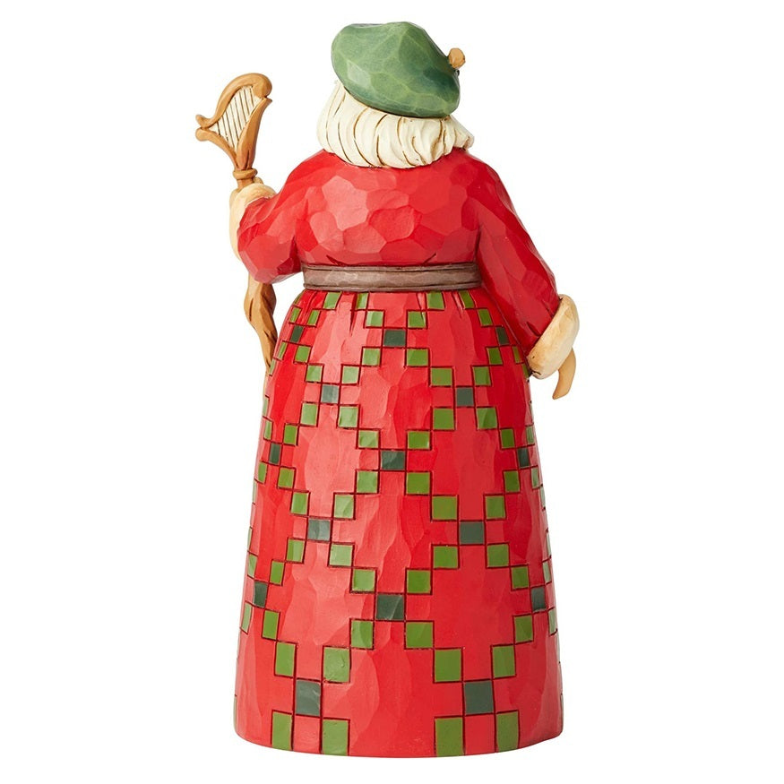 A Jim Shore collectible figurine of a whimsical elderly man seen from the back, wearing a red robe with a green and red geometric pattern on the skirt, a green hat, and holding a gold harp.