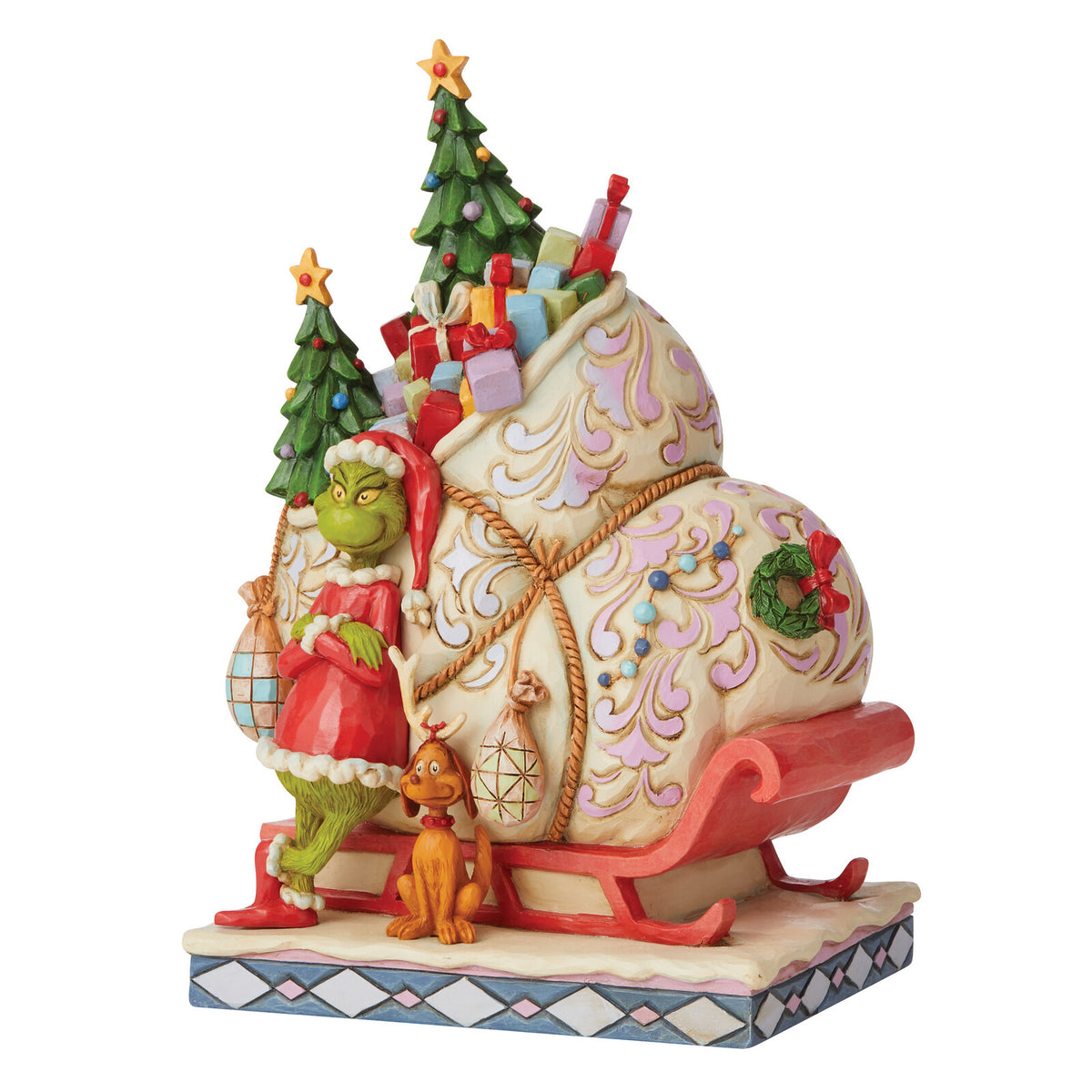 A decorative figurine of the Grinch in a red suit standing beside a large sleigh filled with presents, with two small Christmas trees and a small orange dog on a white studio background.