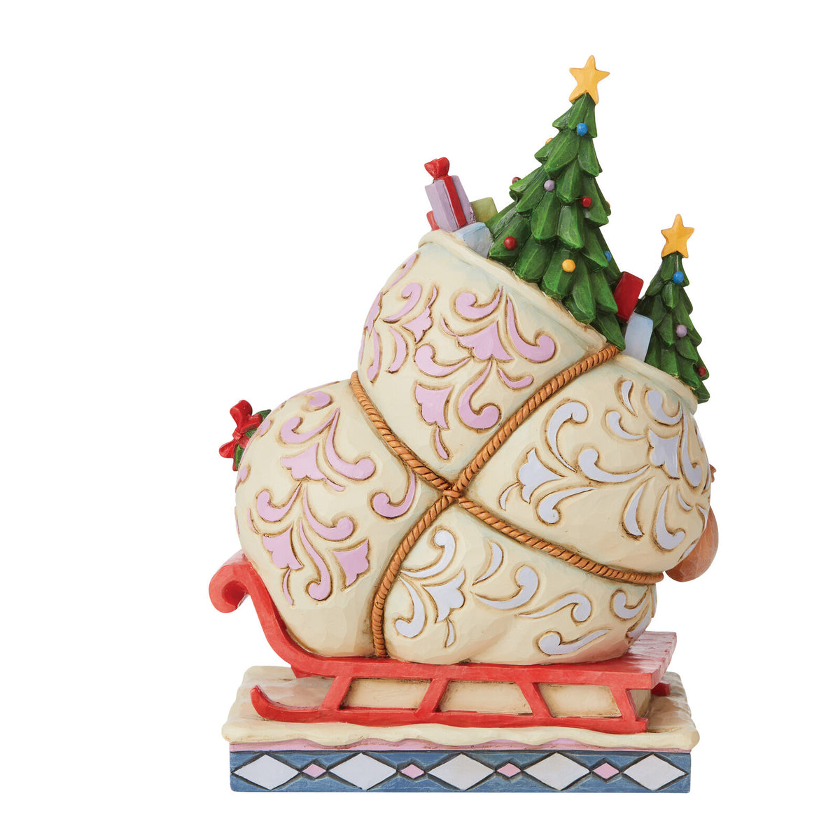 A decorative Christmas Santa sack figurine on a sled, with two small green Christmas trees and gift boxes protruding from the top, shown on a plain white background.