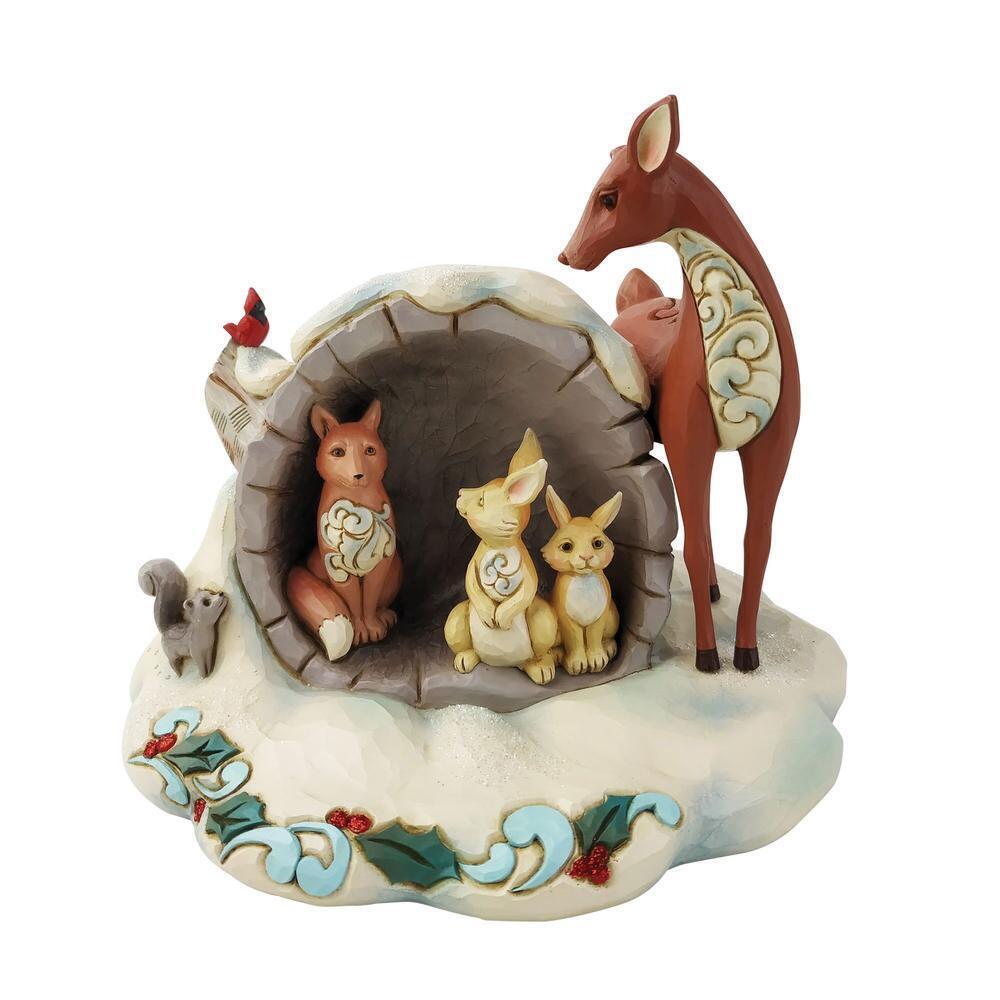 A whimsical winter woodland figurine featuring a brown deer standing beside a cave-like opening where a fox, rabbit, and kitten sit, all decorated with cream scroll motifs. A small red bird perches on the left, and the base is snowy white with blue and green holly accents and red berries.