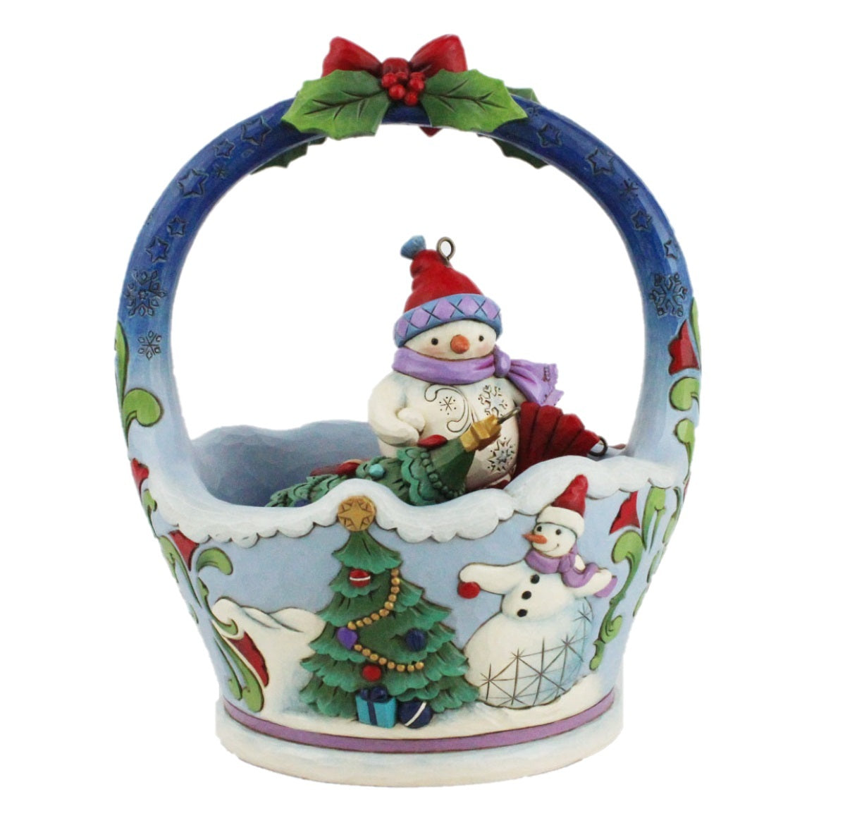 A decorative ceramic Christmas basket ornament featuring snowman figures, a decorated Christmas tree, and a holly leaf and berry accent on the handle, shown against a plain white background.