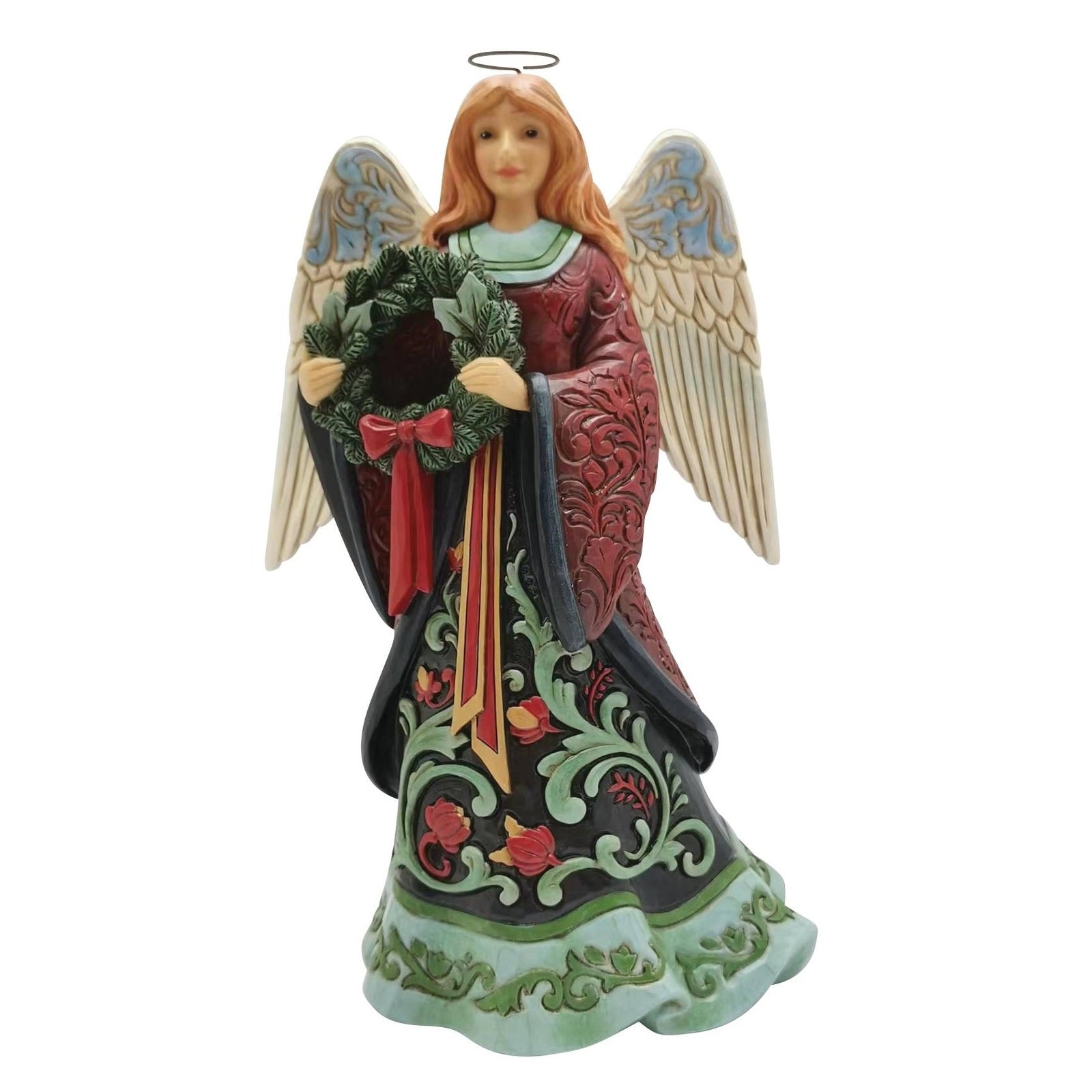An angel Christmas ornament figurine with red hair, holding a green wreath with a red bow. The angel has large beige wings with blue accents and wears a dark red and black robe with green and red floral patterns.