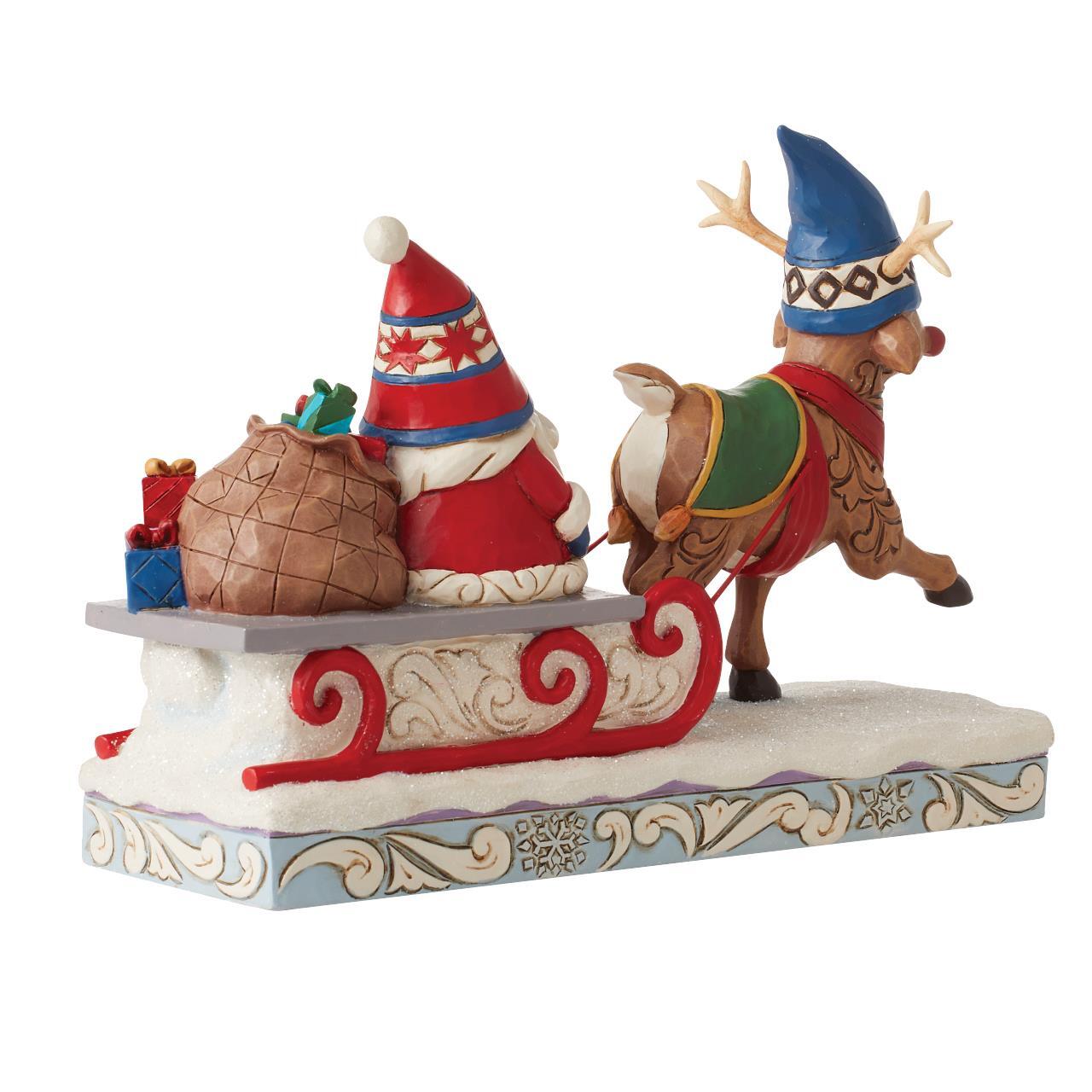 A Christmas figurine depicting Santa Claus in a red hat and suit sitting in a snow-covered sleigh pulled by a brown reindeer wearing a blue hat, on a decorative base against a white background.