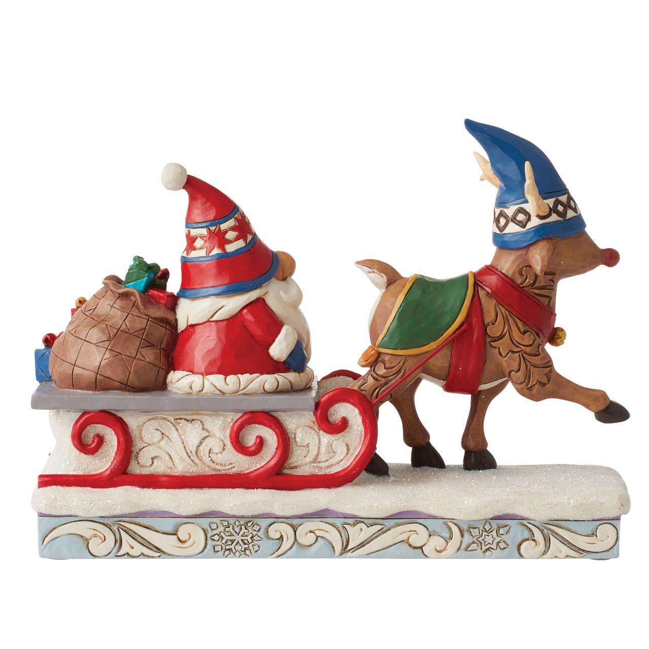 A decorative Christmas figurine showing Santa Claus in a red hat sitting in a red sleigh, pulled by a brown reindeer wearing a blue hat and green and red saddle, on a white and light blue patterned base against a plain white background.
