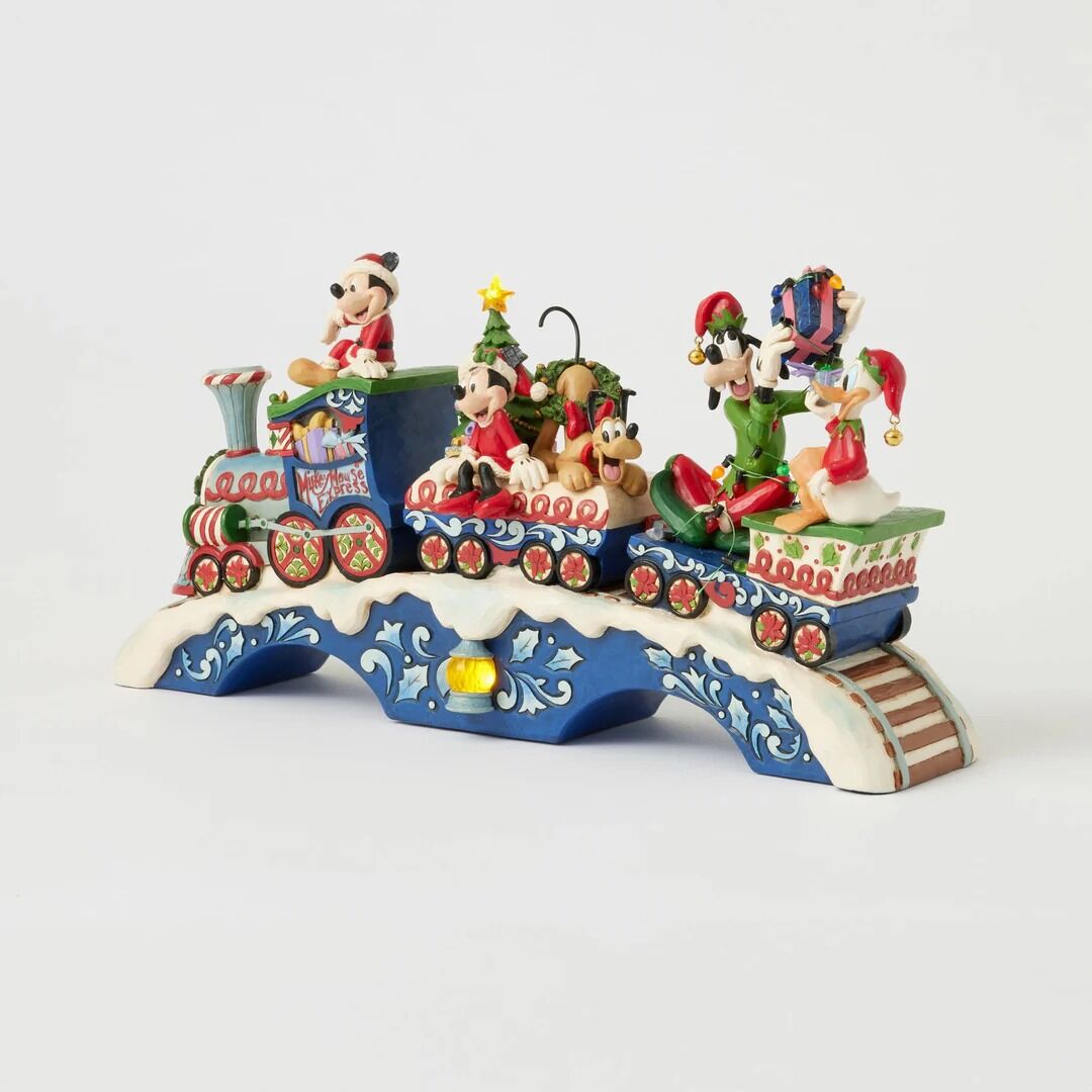 A Disney Christmas-themed decorative train figurine featuring Mickey Mouse, Minnie Mouse, Donald Duck, Goofy, Pluto, and Daisy Duck riding on a snow-covered bridge over a blue track bed, set against a plain light gray background.