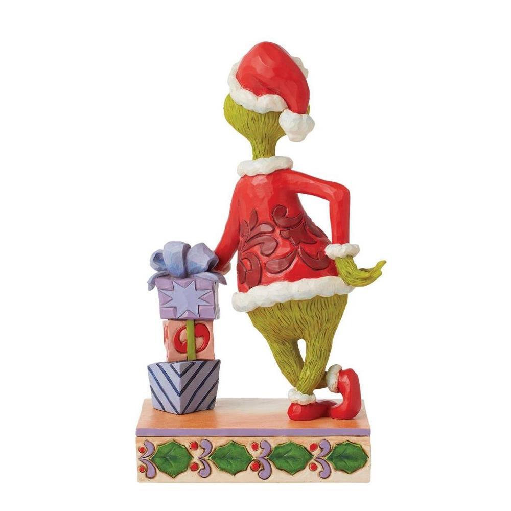 A Grinch figurine wearing a red Santa suit and Santa hat, standing on a decorated base next to wrapped gifts, photographed against a plain white background.