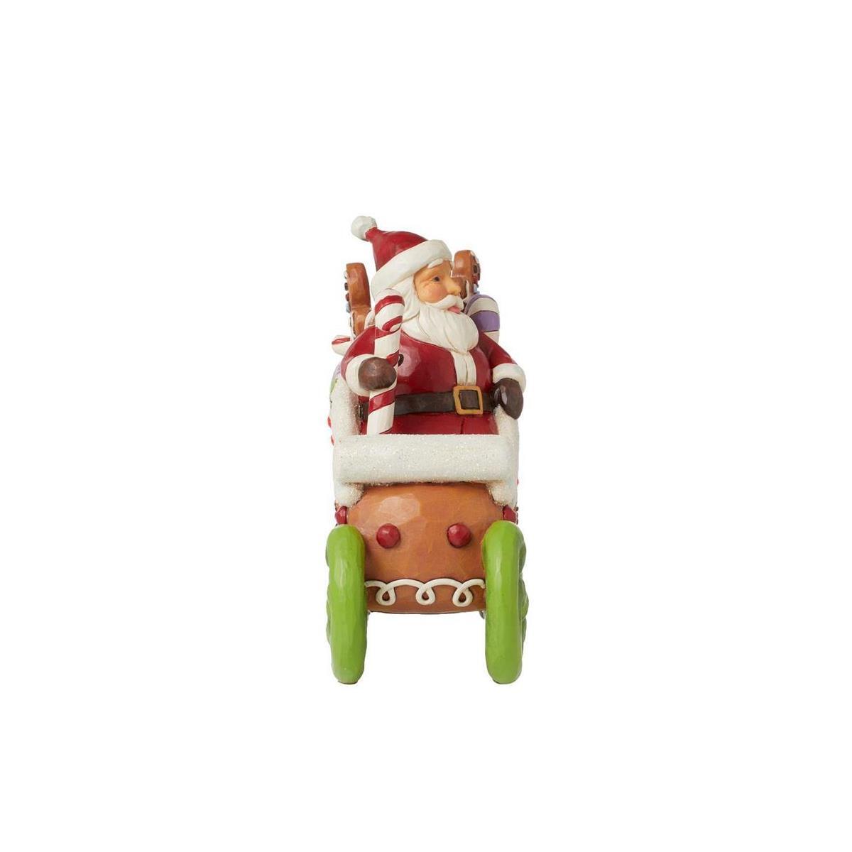 A Santa Claus figurine driving a gingerbread cart, featuring Santa in his red and white suit with a green sleigh base, set against a plain white background.