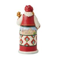 A Christmas-themed ceramic gingerbread man cookie jar with a red hat, white beard, and a decorated body featuring a holiday village scene and diamond patterns.
