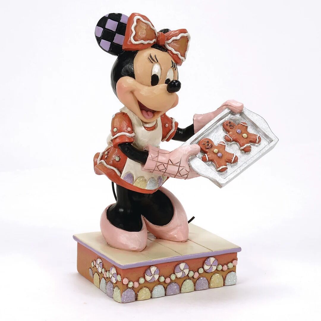 A decorative figurine of Minnie Mouse dressed as a gingerbread woman, holding a tray with gingerbread cookies, set on a decorated rectangular base against a plain white background.